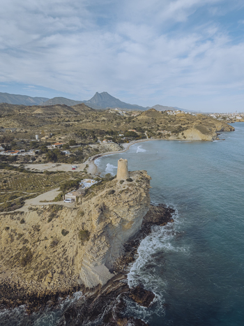 Aerial view of Torre del Xarco on a rugged cliff overlooking the Mediterranean Sea with mountains in the background La Vila Joiosa Comunidad Valenciana Spain.