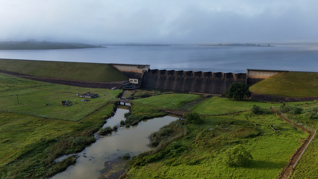 Aerial view of Midmar Dam featuring its concrete spillway and grassy embankments under misty hills and a cloudy sky in Howick KwaZulu Natal South Africa. Aerial view of Midmar Dam featuring its concrete spillway and grassy embankments under misty hills and a cloudy sky in Howick KwaZulu Natal South Africa.
