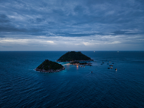 Aerial view of the islands of Ko Tao surrounded by deep blue sea under a dramatic twilight sky with small boats anchored near the shore in Ko Tao Surat Thani Thailand.