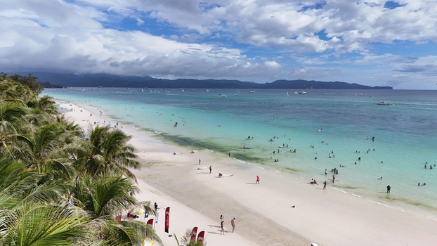 Malay Philippines 02 May 2026 Aerial view of Boracay Island featuring turquoise waters white sand palm trees and people swimming under a cloudy sky.