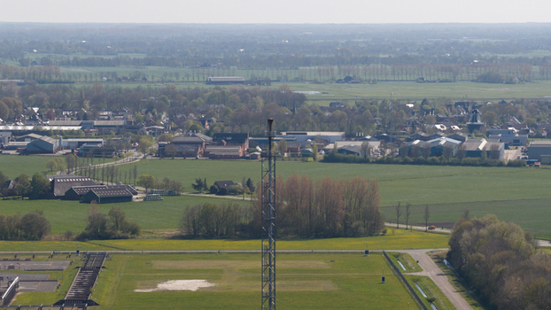 Aerial view of the NAM Grijpskerk UGS facility featuring a tall flare stack surrounded by green fields and the village landscape in Grijpskerk Groningen Netherlands.