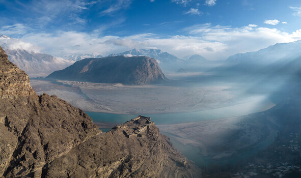 Aerial view of the historic Kharpocho Fort perched on a rocky cliff overlooking the Indus River and the vast valley surrounded by snow capped mountains in Skardu Pakistan.
