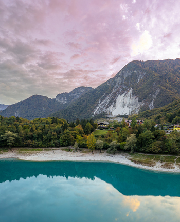 Aerial view of Lago di Tenno with its turquoise water reflecting the surrounding mountains and forest under a soft pink sunset sky in Tenno Trentino Alto Adige Italy.