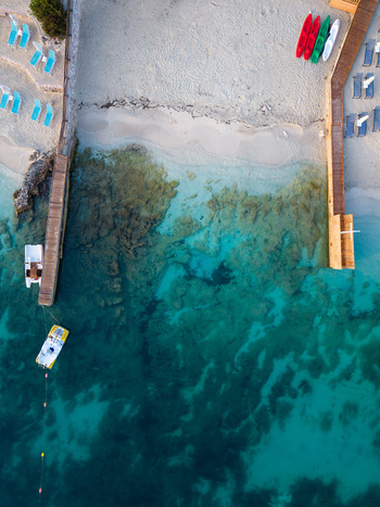 Aerial view of a sandy beach with turquoise water wooden piers colorful kayaks and sun loungers along the coast of Albania.