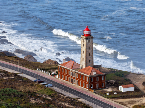 Aerial view of Farol Penedo da Saudade lighthouse with crashing waves on the rocky Atlantic coast and a coastal road in Marinha Grande Leiria Portugal. Aerial view of Farol Penedo da Saudade lighthouse with crashing waves on the rocky Atlantic coast and a coastal road in Marinha Grande Leiria Portugal.