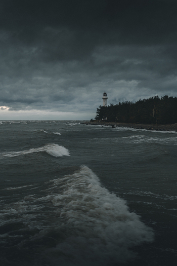 View of Saxby Lighthouse standing on a rocky coastline with stormy waves crashing against the shore under a dark overcast sky in Saxby Laane maakond Estonia.