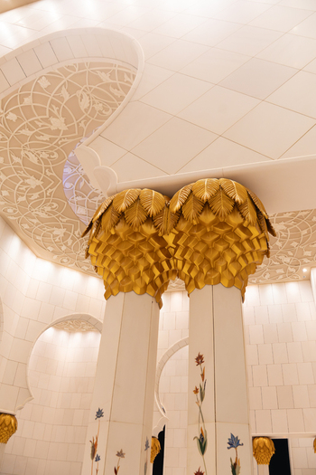 View of the ornate interior of the Sheikh Zayed Grand Mosque featuring marble columns with golden palm capitals and floral inlays in Abu Dhabi Abu Dhabi United Arab Emirates. View of the ornate interior of the Sheikh Zayed Grand Mosque featuring marble columns with golden palm capitals and floral inlays in Abu Dhabi Abu Dhabi United Arab Emirates.
