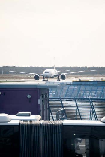 View of a passenger airplane taxiing on the tarmac at Frankfurt Airport with blue metal fencing in the foreground in Frankfurt am Main Hessen Germany. View of a passenger airplane taxiing on the tarmac at Frankfurt Airport with blue metal fencing in the foreground in Frankfurt am Main Hessen Germany.