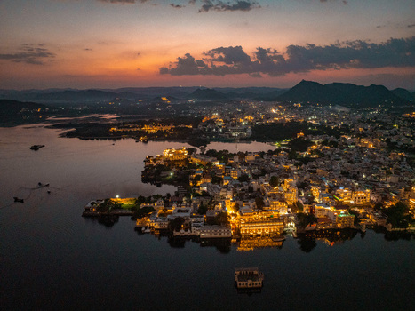 Aerial view of the illuminated City Palace and historic architecture along the shores of Lake Pichola at sunset in Udaipur Rajasthan India.