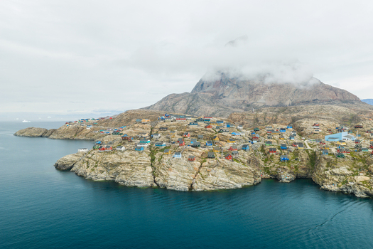 Aerial view of the colorful houses of Uummannaq town nestled on rocky coastal terrain with the iconic Uummannaq mountain shrouded in clouds Uummannaq Kitaa Greenland. Aerial view of the colorful houses of Uummannaq town nestled on rocky coastal terrain with the iconic Uummannaq mountain shrouded in clouds Uummannaq Kitaa Greenland.