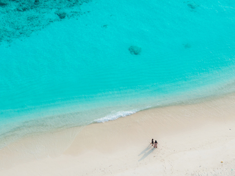 Aerial view of the pristine turquoise ocean gently meeting the soft golden white sandy beach where two figures stroll Hoarafushi Thiladhunmathee Uthuruburi Maldives. Aerial view of the pristine turquoise ocean gently meeting the soft golden white sandy beach where two figures stroll Hoarafushi Thiladhunmathee Uthuruburi Maldives.