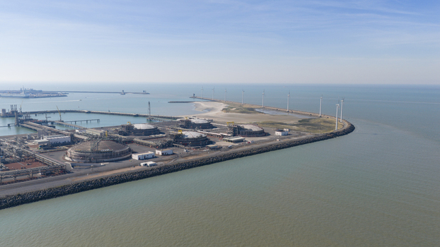 Aerial view of Fluxys LNG Terminal Zeebrugge featuring large storage tanks and a line of wind turbines along the breakwater under a clear blue sky in Brugge Vlaanderen Belgium. Aerial view of Fluxys LNG Terminal Zeebrugge featuring large storage tanks and a line of wind turbines along the breakwater under a clear blue sky in Brugge Vlaanderen Belgium.