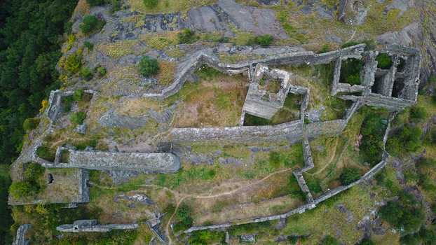 Aerial view of the ancient stone ruins of Montjovet Castle with its weathered walls and towers perched on a rocky hillside surrounded by lush green forest in Montjovet Aosta Valley Italy.