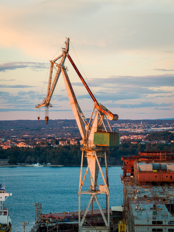 Aerial view of the iconic Uljanik Shipyard crane standing over the industrial waterfront with ships and the cityscape of Pula Croatia. Aerial view of the iconic Uljanik Shipyard crane standing over the industrial waterfront with ships and the cityscape of Pula Croatia.