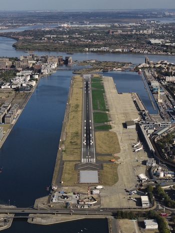 Aerial view of London City Airport with its runway situated between the docks surrounded by urban infrastructure and the River Thames in London England United Kingdom. Aerial view of London City Airport with its runway situated between the docks surrounded by urban infrastructure and the River Thames in London England United Kingdom.
