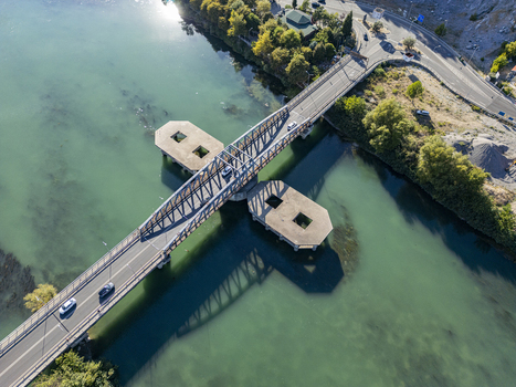 Aerial view of Ura e re e Bunes bridge spanning the turquoise waters of the Buna River with cars driving across and surrounding green vegetation in Shkoder Qarku i Shkodres Albania. Aerial view of Ura e re e Bunes bridge spanning the turquoise waters of the Buna River with cars driving across and surrounding green vegetation in Shkoder Qarku i Shkodres Albania.