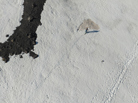 Aerial view of a lone hiker walking across a vast snowfield on the Versante sud dell Etna next to dark volcanic rocks in Nicolosi Sicilia Italy. Aerial view of a lone hiker walking across a vast snowfield on the Versante sud dell Etna next to dark volcanic rocks in Nicolosi Sicilia Italy.
