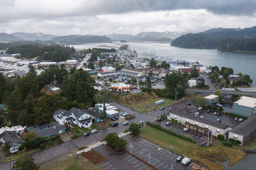 Aerial view of Florence Oregon featuring the coastal town wooded neighborhoods commercial buildings and the Siuslaw River estuary under an overcast sky.