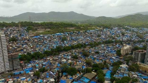 Aerial view of Dharavi Slums showing dense clusters of dwellings with blue tarpaulin roofs surrounded by green hills and modern high rise buildings in Mumbai Maharashtra India. Aerial view of Dharavi Slums showing dense clusters of dwellings with blue tarpaulin roofs surrounded by green hills and modern high rise buildings in Mumbai Maharashtra India.