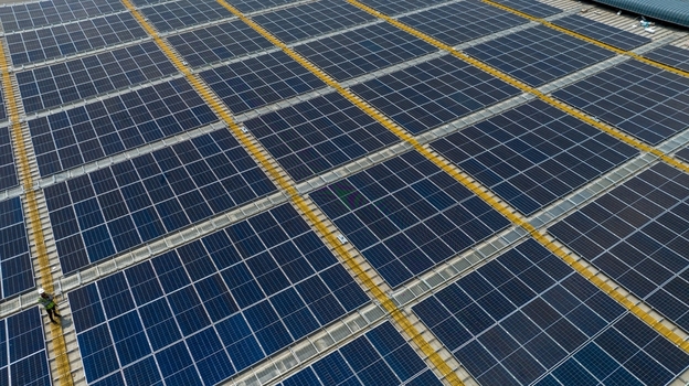 Aerial view of a large warehouse roof covered with rows of solar panels and a worker walking along the edge in Bhiwandi Maharashtra India. Aerial view of a large warehouse roof covered with rows of solar panels and a worker walking along the edge in Bhiwandi Maharashtra India.