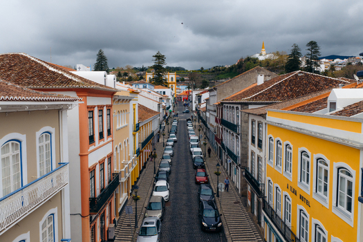 Aerial view of colorful historic buildings and a narrow street with parked cars under an overcast sky in Angra do Heroismo Azores Portugal.