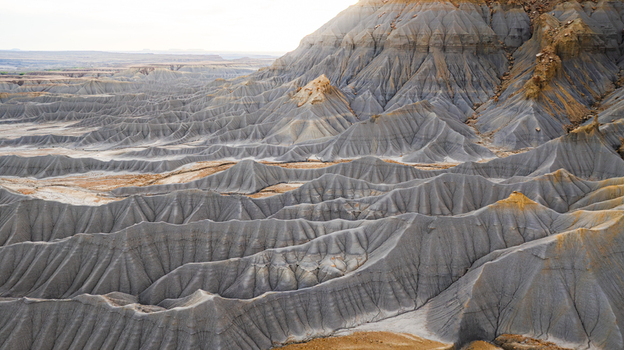 Aerial view of the rugged badlands landscape with intricate grey clay ridges deep erosion patterns and golden hued soil in Hanksville Utah United States.