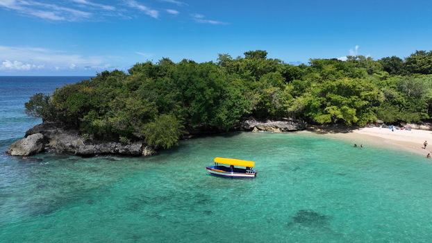 Aerial view of La Casita de Playa with a small boat with a yellow canopy in turquoise water near a lush green coastline in Rio San Juan Maria Trinidad Sanchez Dominican Republic.