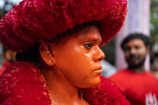Munshiganj Bangladesh 13 April 2025 View of a face vividly painted fiery orange framed by a voluminous textured red headpiece its intense gaze fixed. Munshiganj Bangladesh 13 April 2025 View of a face vividly painted fiery orange framed by a voluminous textured red headpiece its intense gaze fixed.