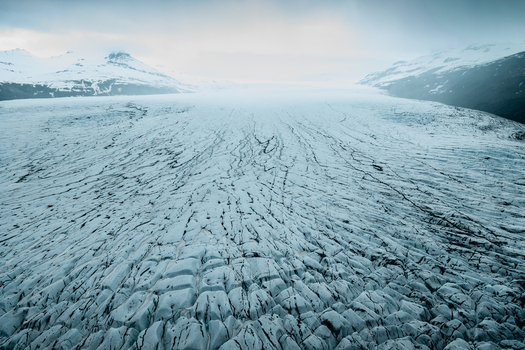 Aerial view of Vatnajokull glacier featuring intricate ice crevasses and textured surfaces surrounded by snow capped mountains in Iceland.