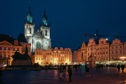 Prague Czechia 03 November 2021 View of the Church of Our Lady before Tyn illuminated at night in the Old Town Square with people walking on the cobblestones. Prague Czechia 03 November 2021 View of the Church of Our Lady before Tyn illuminated at night in the Old Town Square with people walking on the cobblestones.