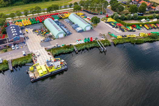 Aerial view of Rijkswaterstaat Harderhaven facility featuring rows of colorful navigation buoys storage warehouses and a work vessel docked at the pier in Zeewolde Flevoland Netherlands.