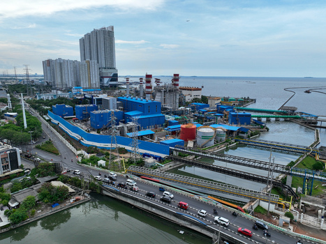 Aerial view of PLTU Pluit power plant with its distinctive blue industrial buildings large storage tanks and nearby high rise residential towers situated along the coast in Kecamatan Penjaringan Daerah Khusus Ibukota Indonesia.