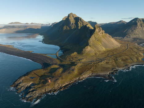 Aerial view of stark mountains meeting the dark sandy shorelines a lone lighthouse standing sentinel against the vast ocean Hvalnes Sveitarfélagið Hornafjörður Iceland. Aerial view of stark mountains meeting the dark sandy shorelines a lone lighthouse standing sentinel against the vast ocean Hvalnes Sveitarfélagið Hornafjörður Iceland.