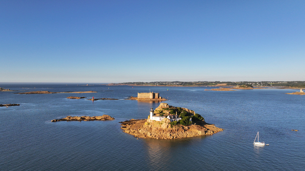 Aerial view of &Icirc;le Lou&euml;t s white lighthouse and the ancient Ch&acirc;teau du Taureau fortress standing guard amidst the tranquil deep blue waters. Carantec Brittany France.