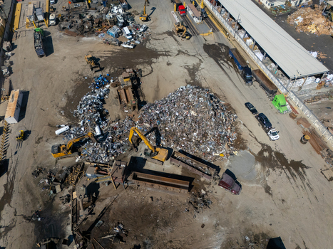 Aerial view of a scrap metal recycling facility with large piles of metal yellow excavators and industrial trucks in a yard in Carson California United States.