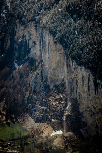 View of a towering cliff face streaked with pale waterfalls under the dark forest canopy a symphony of stone water and verdant life Lauterbrunnen Switzerland. View of a towering cliff face streaked with pale waterfalls under the dark forest canopy a symphony of stone water and verdant life Lauterbrunnen Switzerland.