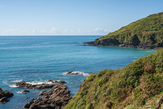 View of the rugged coastline along the South West Coastal Path overlooking the turquoise waters of Portnadler Bay in Looe Cornwall United Kingdom. View of the rugged coastline along the South West Coastal Path overlooking the turquoise waters of Portnadler Bay in Looe Cornwall United Kingdom.