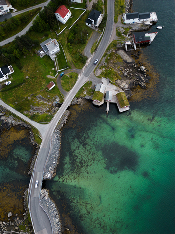 Aerial view of the coastal village of Reine featuring traditional houses grass roofed cabins and turquoise water along the rocky shoreline in Reine Nordland Norway.