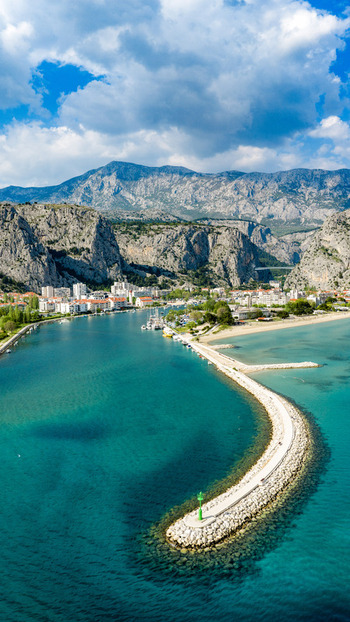 Aerial view of the Cetina river mouth a curved stone breakwater and rugged limestone mountains in Omis Split Dalmatia County Croatia. Aerial view of the Cetina river mouth a curved stone breakwater and rugged limestone mountains in Omis Split Dalmatia County Croatia.