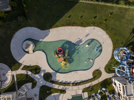 Aerial view of a water park featuring a turquoise pool with colorful slides a central play structure and paved walkways surrounded by green lawns in Bulgaria. Aerial view of a water park featuring a turquoise pool with colorful slides a central play structure and paved walkways surrounded by green lawns in Bulgaria.