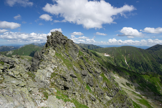 View of Tri kopy in Western Tatras with hikers on the jagged rocky ridge under a blue sky with white clouds in Ziar Zilina Region Slovakia. View of Tri kopy in Western Tatras with hikers on the jagged rocky ridge under a blue sky with white clouds in Ziar Zilina Region Slovakia.