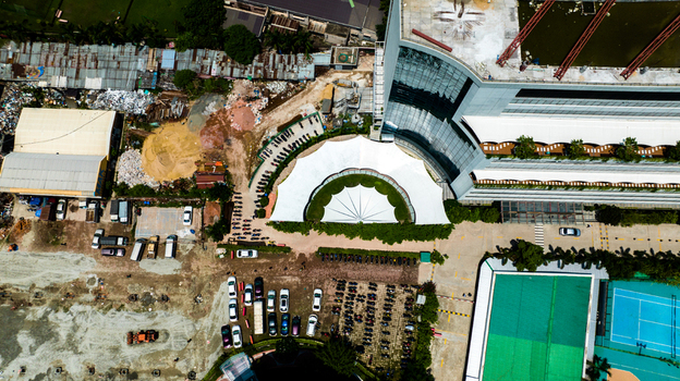 Aerial view of a modern building with a large white semi circular canopy adjacent parking area and tennis court in Dhaka Dhaka Division Bangladesh. Aerial view of a modern building with a large white semi circular canopy adjacent parking area and tennis court in Dhaka Dhaka Division Bangladesh.