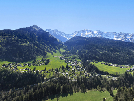 Saint Gervais les Bains France 30 April 2026 Aerial view of the mountain village of Saint Gervais les Bains surrounded by lush green meadows dense pine forests and snow capped Alpine peaks.