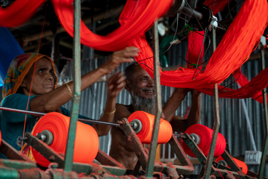Joypurhat Bangladesh 22 September 2026 View of a woman and a man working with bright orange yarn on a textile machine in a workshop. Joypurhat Bangladesh 22 September 2026 View of a woman and a man working with bright orange yarn on a textile machine in a workshop.