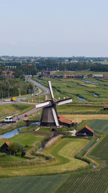 Aerial view of the historic windmill in Schermerhorn surrounded by lush green fields winding canals and a road with traffic in Schermerhorn North Holland Netherlands. Aerial view of the historic windmill in Schermerhorn surrounded by lush green fields winding canals and a road with traffic in Schermerhorn North Holland Netherlands.