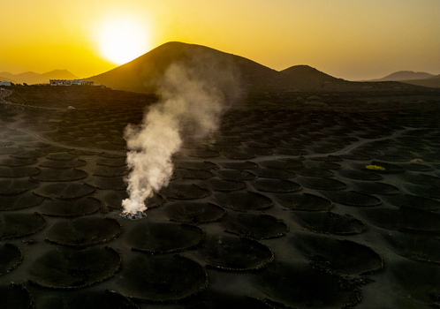 Aerial view of volcanic craters and rising smoke under a golden sunset sky in Lanzarote Canarias Spain. Aerial view of volcanic craters and rising smoke under a golden sunset sky in Lanzarote Canarias Spain.