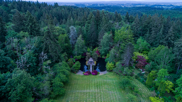 Aerial view of a serene garden with a central pond and gazebo surrounded by dense evergreen forests and manicured lawns in Portland Oregon United States. Aerial view of a serene garden with a central pond and gazebo surrounded by dense evergreen forests and manicured lawns in Portland Oregon United States.