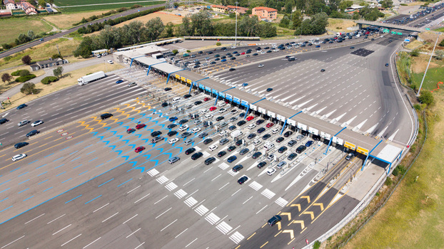 Aerial view of the Autostrada A1 toll plaza with multiple vehicle lanes traffic flow and surrounding green landscape in Melegnano Lombardy Italy.