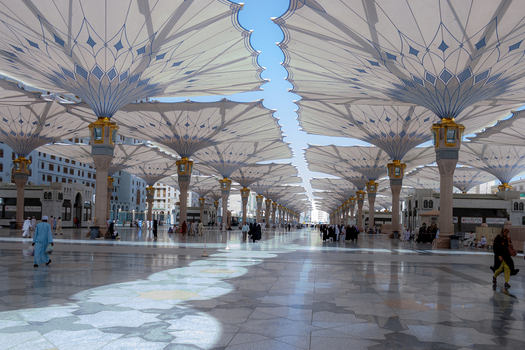 View of Al Masjid e Nabawi with large retractable umbrellas providing shade over the marble courtyard with people walking in Madinah Al Madinah Province Saudi Arabia.