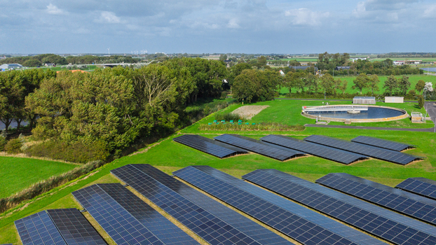 Aerial view of solar panels installed in a green field next to a water treatment facility with circular tanks and surrounding trees in Schagerbrug Noord Holland Netherlands. Aerial view of solar panels installed in a green field next to a water treatment facility with circular tanks and surrounding trees in Schagerbrug Noord Holland Netherlands.